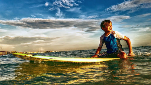 Boy on surfboard in sea against sky