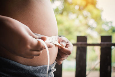 Midsection of pregnant woman measuring abdomen with tape measure