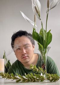 Portrait of young asian man with aromatherapy diffuser, peace lilies in vase and branches.