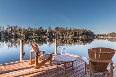 Chairs and table by lake against clear sky