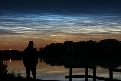 Silhouette man standing by lake against sky during sunset