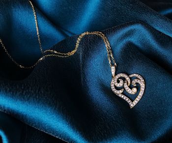 Close-up of heart shape pendant with chain on blue fabric