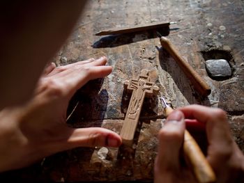 Close-up of man hand carving wooden cross at table