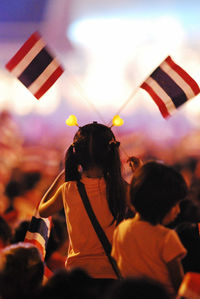 Rear view of girl holding thai flags during festival at night