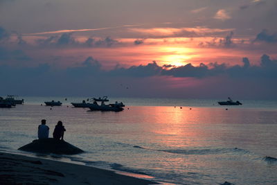 Silhouette people on sea against sky during sunset