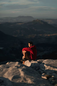 Man sitting on rock against mountain range