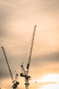 Low angle view of cranes against sky at sunset