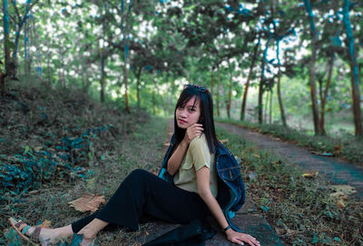 Portrait of beautiful young woman sitting on land in forest