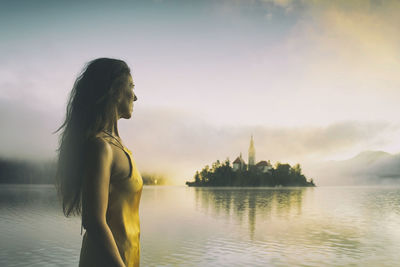 Woman in gray coat watching a sunrise among the fog on the shores of lake bled, slovenia vi