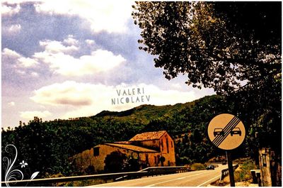 Road sign by trees against sky in city