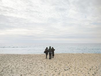 Rear view of men standing on beach against sky