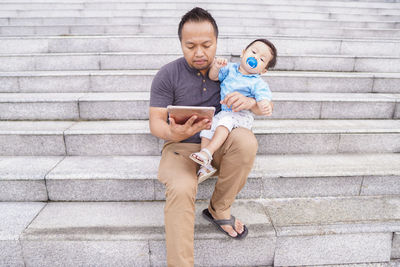 Full length of a man using mobile phone while sitting on staircase