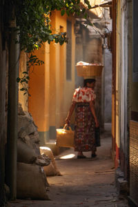 Rear view of woman with wicker basket on head amidst houses