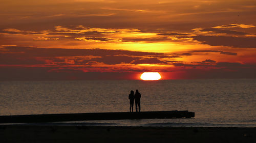 Silhouette people standing by sea against sky during sunset