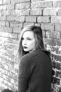 Woman sitting by brick wall