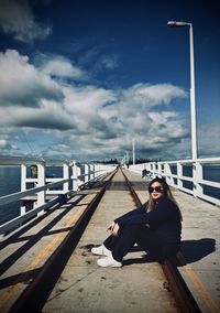Rear view of woman sitting on pier against sky