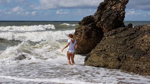 Rear view of woman by rock formations in sea