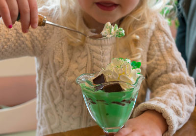 Midsection of girl with ice cream on table at home