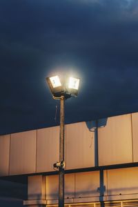 Low angle view of illuminated floodlight against cloudy sky at night