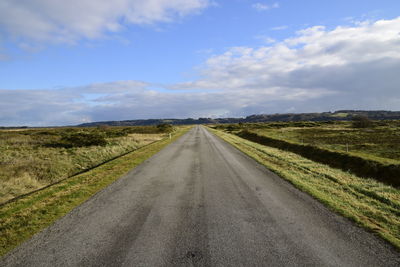 Empty road amidst field against sky