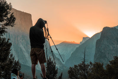 Rear view of person photographing while standing against mountain during sunset