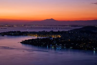 Illuminated city by sea against romantic sky at sunset