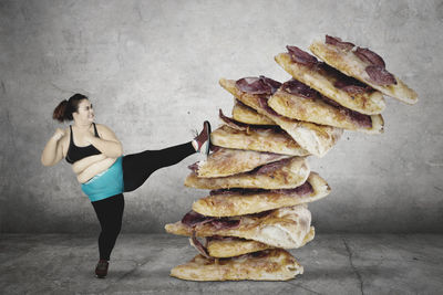 Digital composite image of woman kicking stacked pizza slices against wall