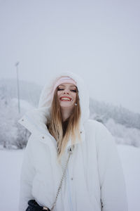 Portrait of young woman standing on snow covered field against clear sky