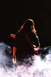 Rear view of woman with arms raised against black background