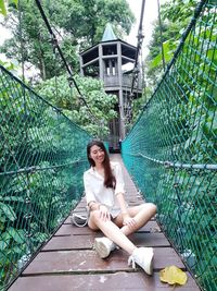 Portrait of woman sitting on fence against plants