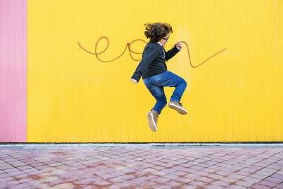 Side view of teenage boy jumping against yellow wall