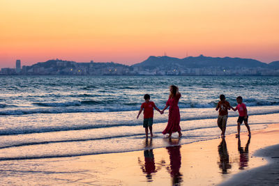 People on beach against sky during sunset