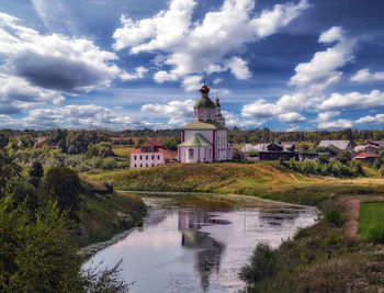 Romantic cloudy sky over summer suzdal city with residential houses, orthodox church and river