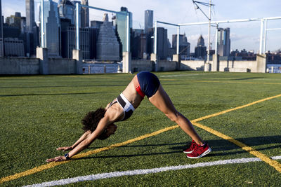 Side view of female athlete practicing downward facing dog position on grassy field