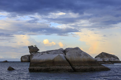 Rocks by sea against sky during sunset