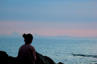 Rear view of woman sitting on rock and looking at view during sunset