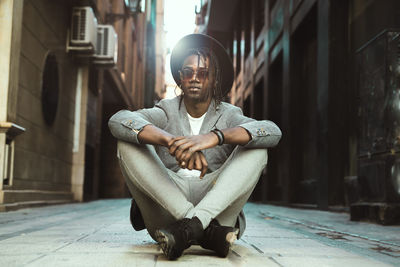 Portrait of young man sitting on sidewalk in city