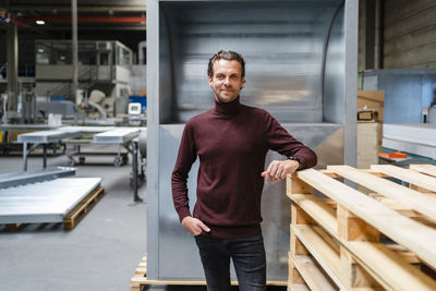 Male professional with hand in pocket standing by stack of wooden pallets