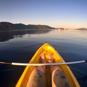 Low section of man kayaking in lake against clear sky