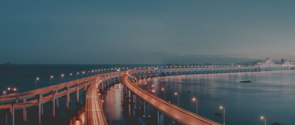 Illuminated bridge over river against sky at night