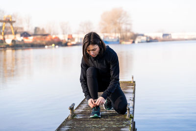 Young female runner is tying her shoes on a harbor quay in the morning - health and wellness concept