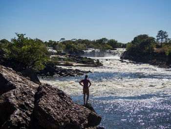 Man standing on rock at ngonye waterfall against clear sky, zambia