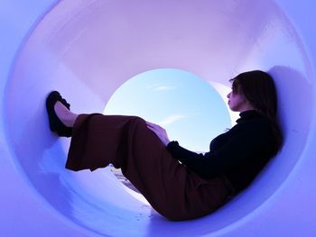 Side view of woman sitting in tube against blue sky