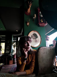 Young woman looking away while sitting in illuminated room