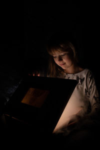 Cute girl holding illuminated box in darkroom