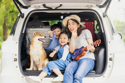 Happy family with shiba inu dog near car outdoors. a family with a mother, daughter and son 