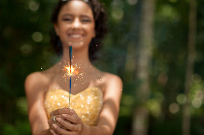 Portrait of smiling woman holding sparkler outdoors