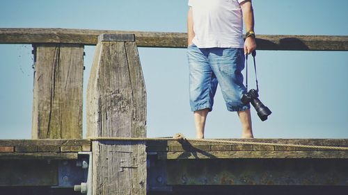 Low section of man standing on railing against sky