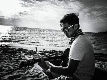 Close-up of man in sunglasses playing guitar at beach against sky