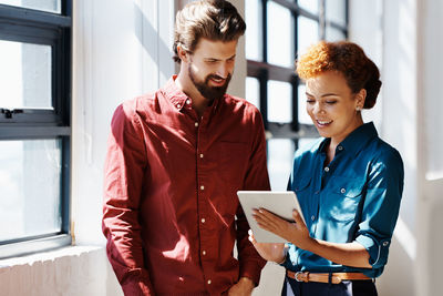 Young couple holding smart phone while standing on laptop